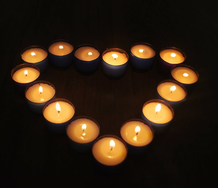 Tea light candles form a heart shape, glowing brightly on a dark surface.