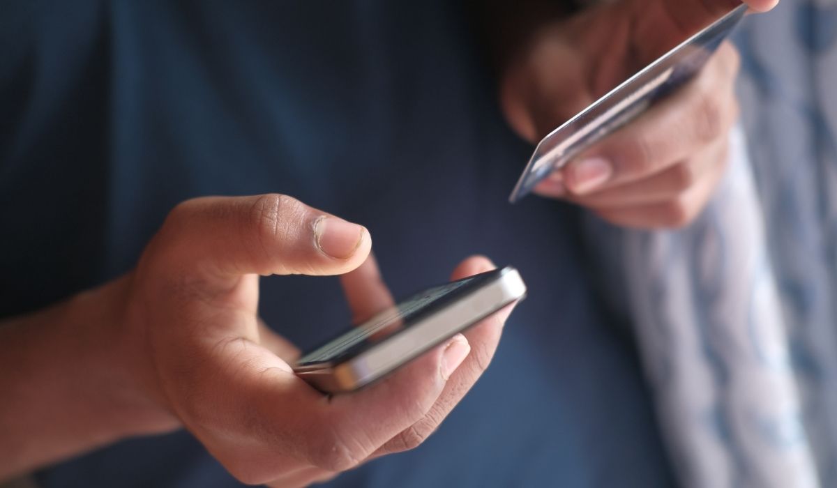 A person's hands are holding a smartphone and a credit card, appearing to be preparing for an online transaction.
